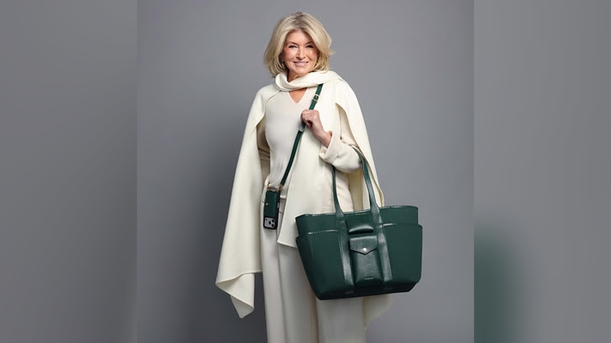 Martha Stewart models her exclusive Bandolier collection featuring a forest-green luxury tote and matching crossbody phone case with an elegant cream ensemble.